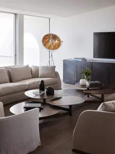 A modern living room featuring metal and wood furniture, minimalist design, and a floor lamp with a gold shade.