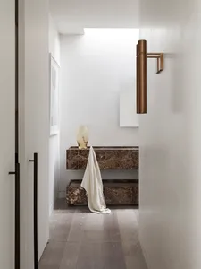 A modern marble bathroom with a minimalist design featuring a vase on a counter and a towel draped over the edge.