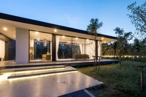 A modern minimalist residential exterior with large glass windows and stone accents.
