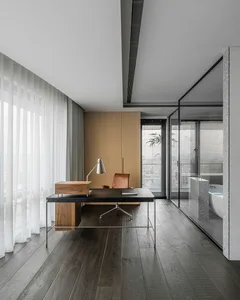 Modern office space with a wooden desk, leather chair, and lamp, featuring a glass-walled bathroom and large windows with she
