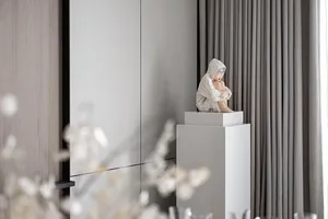 A minimalist interior with a statue of a person sitting on a pedestal.