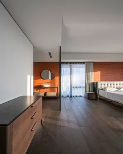 A modern bedroom with a wooden floor, a white bed, and a sink in the background.