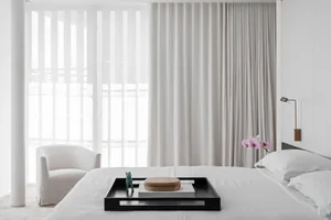 A minimalist bedroom with a white bed, white curtains, and a black tray with decorative items.