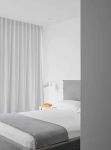 Modern minimalist bedroom with a bed featuring a grey textured throw and a white headboard.