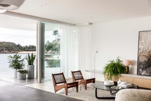 Modern minimalist living room with wood accents, white sheer curtains, and a view of a serene outdoor area.