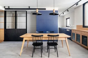 Modern dining room featuring wooden furniture, black chairs, and a blue accent wall.