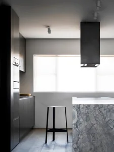 A modern kitchen featuring a marble countertop under natural light from a large window.