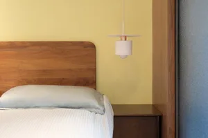 A modern minimalist bedroom featuring a white headboard on a wooden frame set against a yellow and blue wall.
