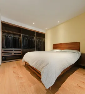 Modern minimalist bedroom featuring a wooden bed frame and a glass closet filled with clothes.