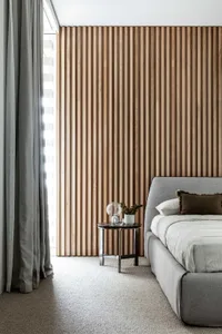 Modern minimalist bedroom featuring a grey upholstered bed with wooden slat paneling on the wall.