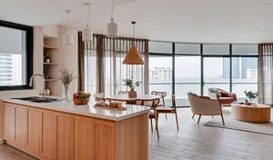 A modern minimalist kitchen with a wooden island, white marble countertops, and glass windows overlooking the city.