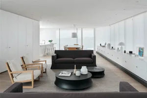 A modern minimalist living room with white walls, dark furniture, and black coffee tables.