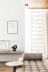 Modern residential living space with concrete walls, sheer curtains, marble coffee table, and grey tufted sofa