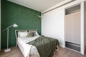 Modern, minimalist bedroom featuring a green accent wall, white bedding, and a wooden bed frame.