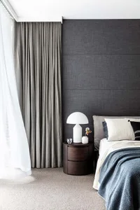A modern minimalist bedroom featuring a textured dark grey wall, taupe curtains, and a bed with neutral tones.