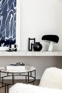 A modern, minimalist setting with a round marble side table featuring a metal frame, accompanied by a black and white abstrac