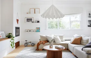 A minimalist living room with a neutral color palette, featuring a white sofa, a round wooden coffee table, and a pendant lig