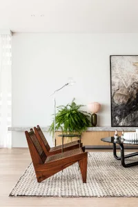A modern living room featuring wooden furniture, a large potted plant, and a abstract painting.