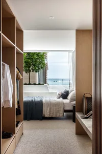 Modern minimalist bedroom with a walk-in closet, glass door, and ocean view.