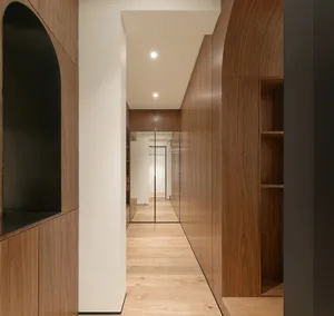 A minimalist corridor with wooden walls and flooring, featuring arches and recessed lighting.