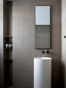 A minimalist bathroom featuring ceramic tile walls, a modern pedestal sink, and a tall rectangular mirror.