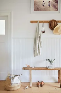 A minimalist entryway featuring a wood hanging hook, bench, and basket