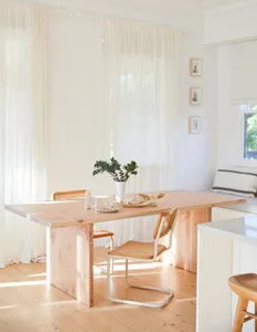 A minimalist kitchen with wooden elements, including a table and chairs, a vase with greenery, and a bread loaf.