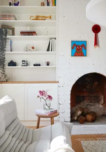 A minimalist living room with a white couch, wooden coffee table, and a white brick fireplace.