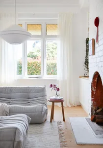 A minimalist living room with light wood flooring, white curtains, and a gray sofa.