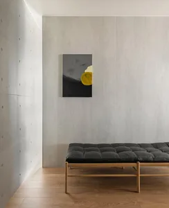 A minimalist living space with a concrete structure, a black cushioned bench, and a yellow abstract painting on the wall.