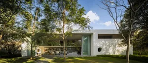 A modern residential interior featuring glass doors and concrete furnishings, surrounded by greenery.
