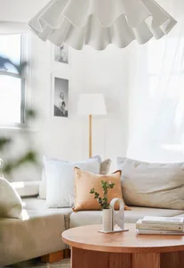 A minimalist living room featuring a light-colored fabric sofa, round wooden coffee table, and decorative elements like a fri