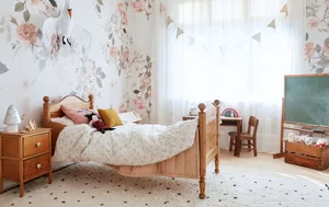 A bedroom with white curtains, floral wallpaper, wooden furniture, and items on the floor.
