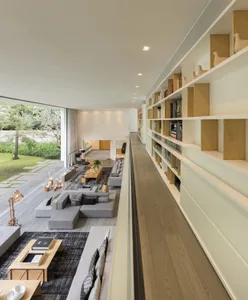 Modern living room with a long bookshelf filled with books and decorative objects, featuring light-colored wood flooring and 