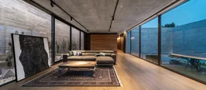 Modern living room featuring a concrete wall, wood floor, and large windows.