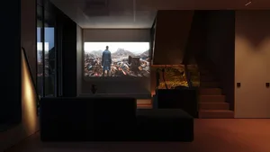 A modern living room with a couch, a person sitting on the couch watching a movie on a large screen.