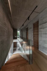 A minimalist home interior with concrete walls, glass railings, and wooden stairs.
