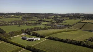 Aerial view of a modern farmhouse with wooden exterior, stone accents, and large glass windows.