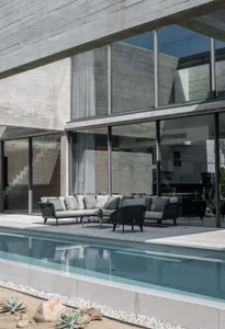 Modern minimalist landscape featuring concrete poolside seating and large glass windows.