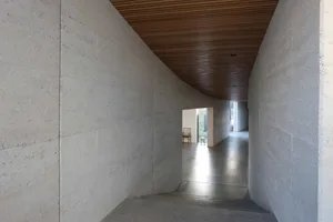 Modern minimalist interior space featuring concrete walls and wooden ceiling.