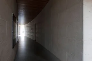 A modern interior space featuring a concrete wall and floor, with a curved ceiling and framed artwork.