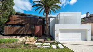 Modern residential house with wooden and metallic exterior, surrounded by greenery and palm trees.