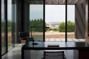 A spacious, modern study room featuring glass windows, a sleek black table, and a comfortable chair with a view of the countr