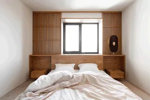 Minimalist bedroom featuring a bed with white bedding and a wooden headboard with built-in shelves.