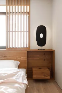 A minimalist bedroom with a wooden nightstand featuring a unique black sculptural lamp.