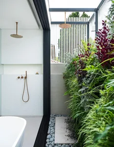 A minimalist modern bathroom featuring concrete surfaces, glass accents, metallic fixtures, and landscaped plants.