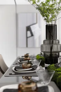 A minimalist dining setting with glass decor and green plants.