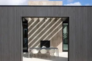 A modern outdoor dining space featuring concrete walls and a metal table with white chairs.