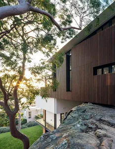 Modern house exterior with wooden cladding and glass windows on a rocky terrain.
