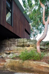 A modern house with a wood exterior built into a rocky cliff side.
